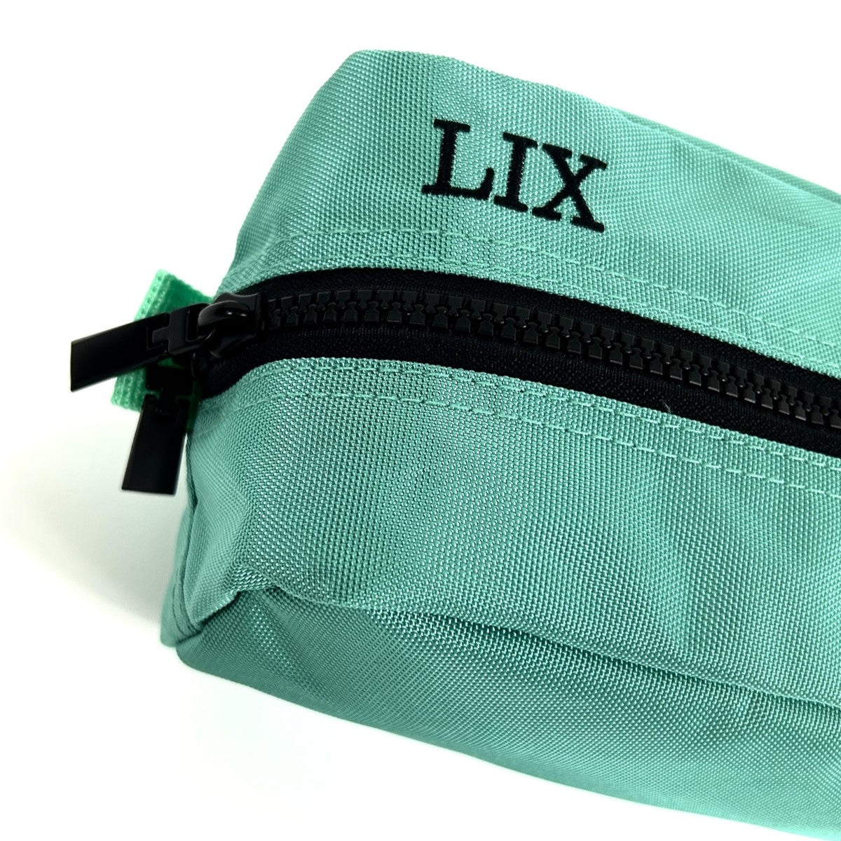 Trousse de voyage de couleur bleue turquoise conçu par Lix design une entreprise québécoise. Fais de matières recyclées, de bouteilles de plastique post consommation. Avec logo embossé dans un badge en cuir synthétique de couleur brune. Lix brodé en noir sur le dessus. Durable et écoresponsable. Étui bleu turquoise. Backpack made in canada. Lix. Sac a dos Canada