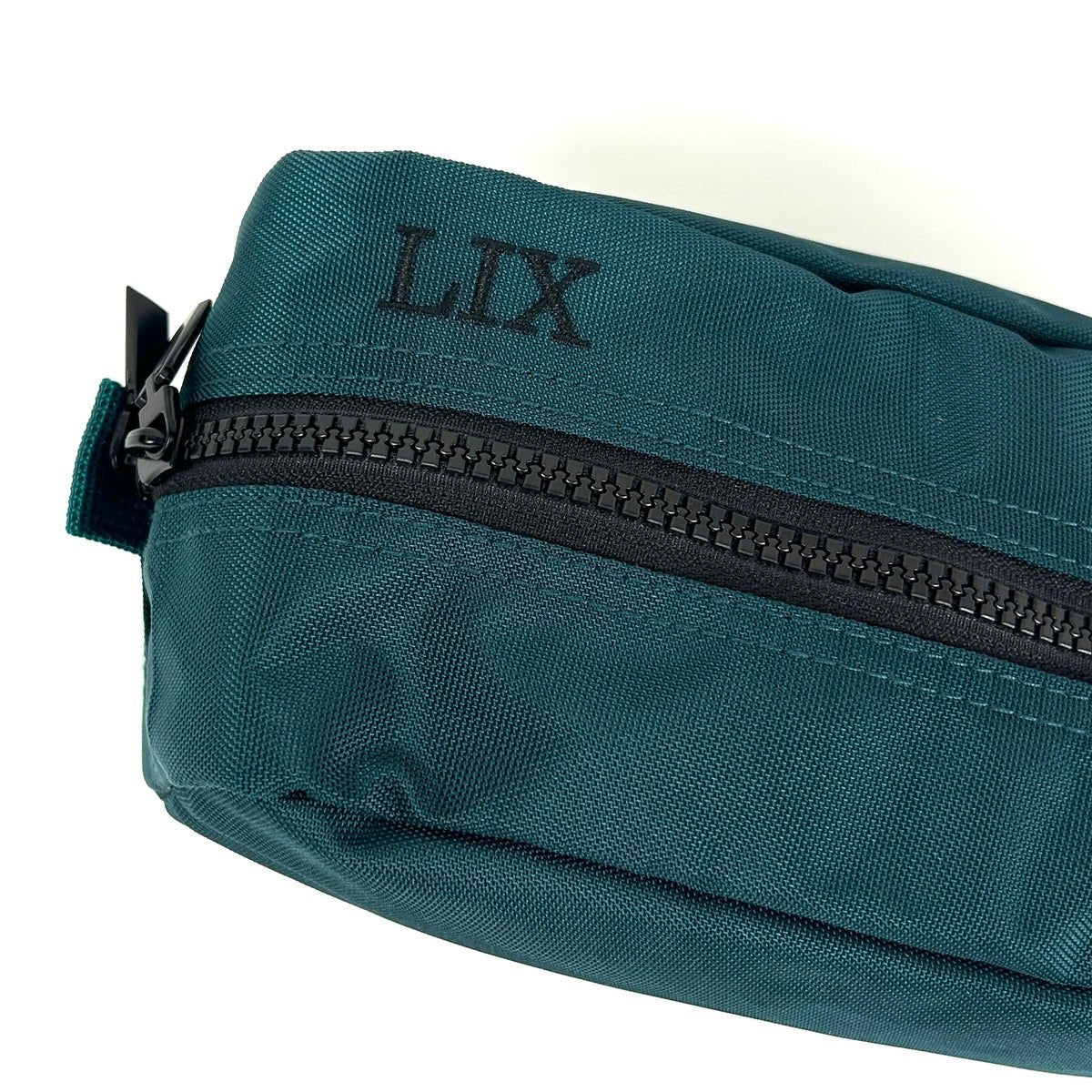 Trousse de voyage de couleur verte émeraude conçu par Lix design une entreprise québécoise. Fais de matières recyclées, de bouteilles de plastique post consommation. Avec logo embossé dans un badge en cuir synthétique de couleur brune. Lix brodé en noir sur le dessus. Durable et écoresponsable.  Étui.