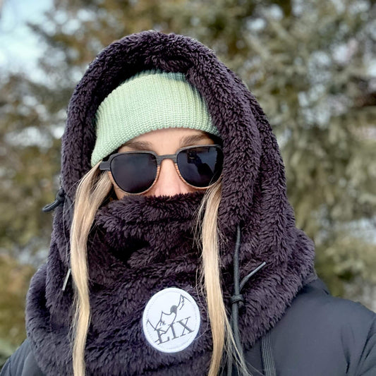 Rider hood de couleur noir avec capuche ajustable et cache-cou intégré. Mountain hood noir par dessus casque de ski. Rider hood Lix.