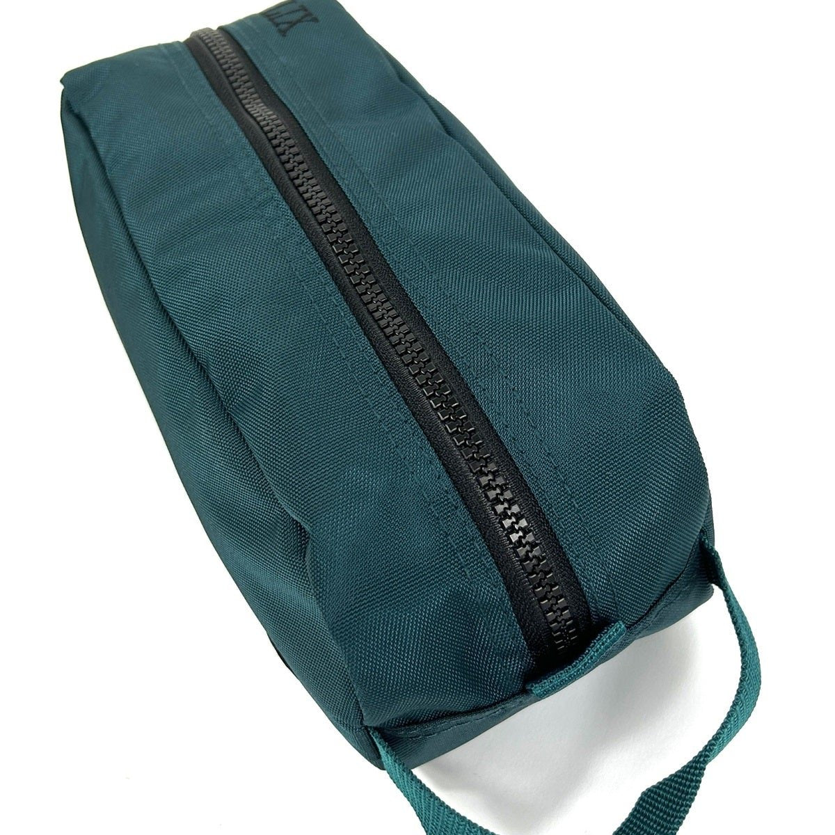 Trousse de voyage de couleur verte émeraude conçu par Lix design une entreprise québécoise. Fais de matières recyclées, de bouteilles de plastique post consommation. Avec logo embossé dans un badge en cuir synthétique de couleur brune.