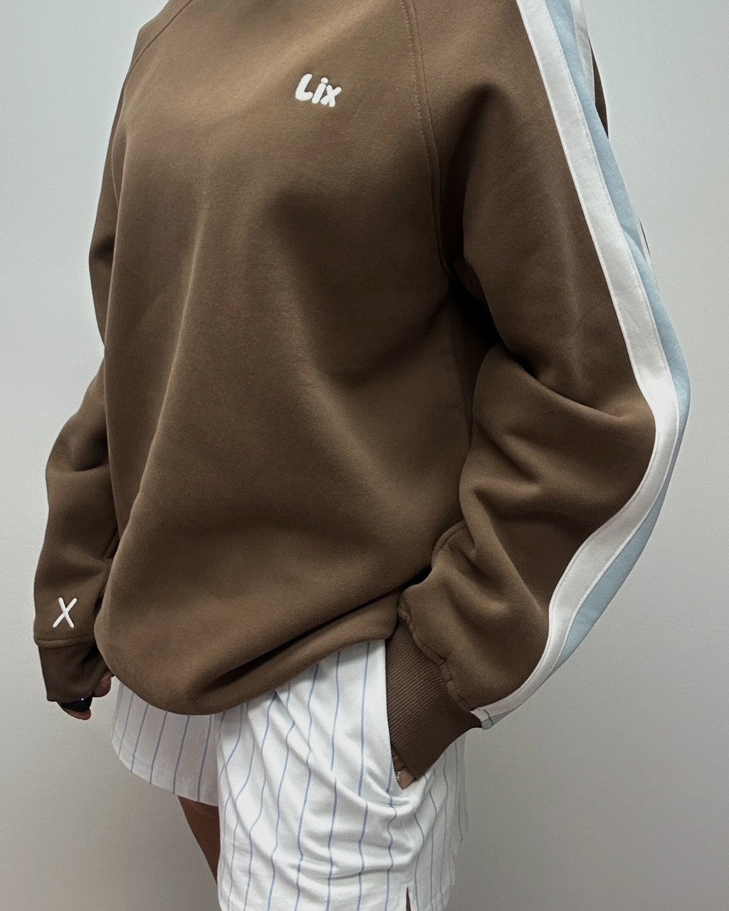 Crewneck brun avec broderie et rayure blanche et bleu sur les manches. Chandail brun avec manche de style raglan. 