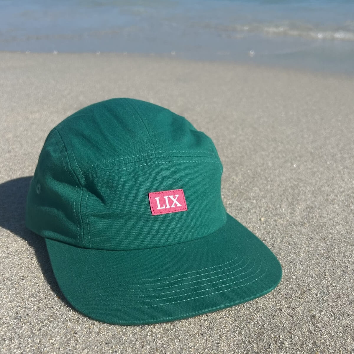 Casquette de couleur vert avec logo rose à 5 panneaux fait de matière recyclées. chapeau de plage vert et rose. 