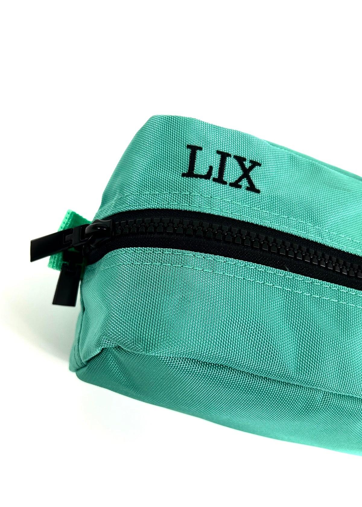 Trousse de voyage de couleur bleue turquoise conçu par Lix design une entreprise québécoise. Fais de matières recyclées, de bouteilles de plastique post consommation. Avec logo embossé dans un badge en cuir synthétique de couleur brune. Lix brodé en noir sur le dessus. Durable et écoresponsable. Étui bleu turquoise. 