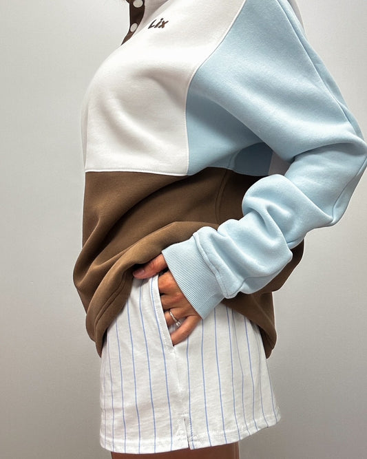 Short blanche en tissu confortable avec rayure bleu et poches sur les côtés. Crewneck avec bouton sur le devant de couleur colorblock blanc bleu et brun. Ajustable à la taille, manche longue. 