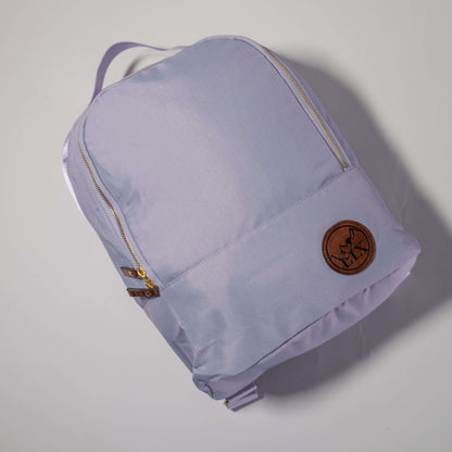 Sac à dos couleur lilas pale de conception éco-responsable. Badge en cuir synthétique végan de couleur brune avec le logo Lix design embossé en noir. Languette de fermeture éclaire en cuir végan brun avec Lix inscrit en noir.