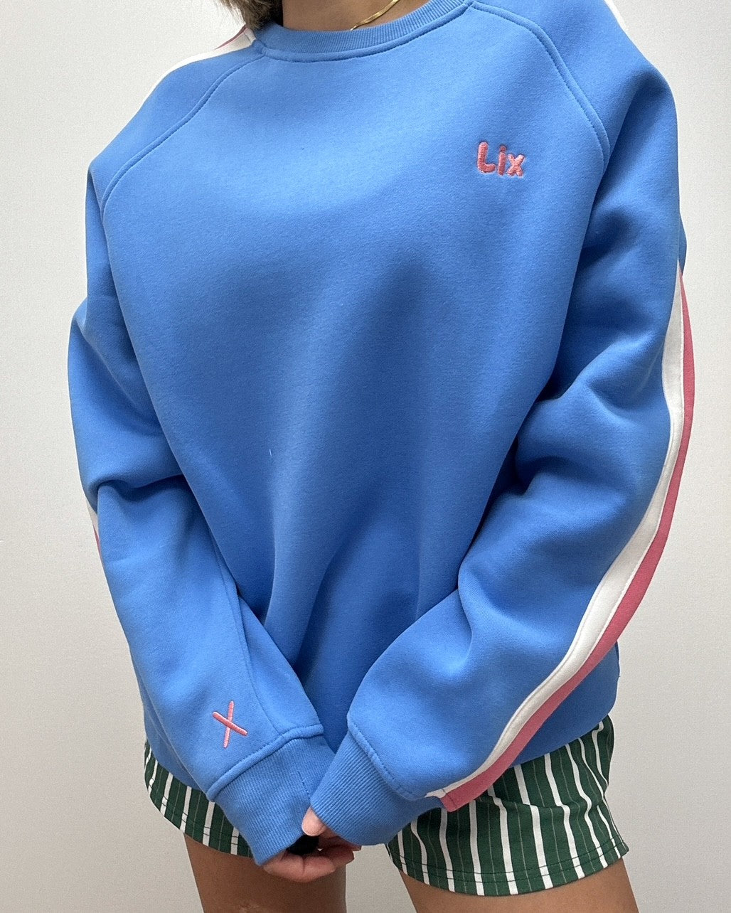Crewneck bleu avec broderie rose de style raglan avec rayure blanche et rose sur les manches. Conçu au Québec pour les femmes et hommes de 25-45 ans. 