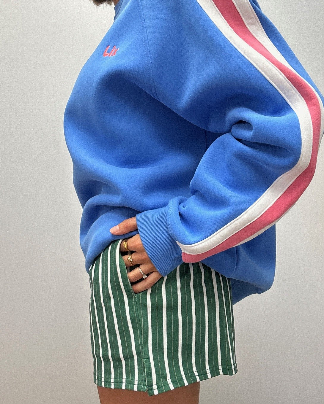 Outfit pour femme de style summer vibe des années 90 rétro vintage. Crewneck bleu avec rayure rose et blanche. Short verte avec rayure blanche et poches sur les côté. 