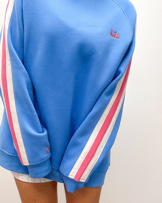 Crewneck bleu avec broderie lix rose sur la poitrine et un X brodé sur la manche. Manche raglan avec rayure blanche et rose. 